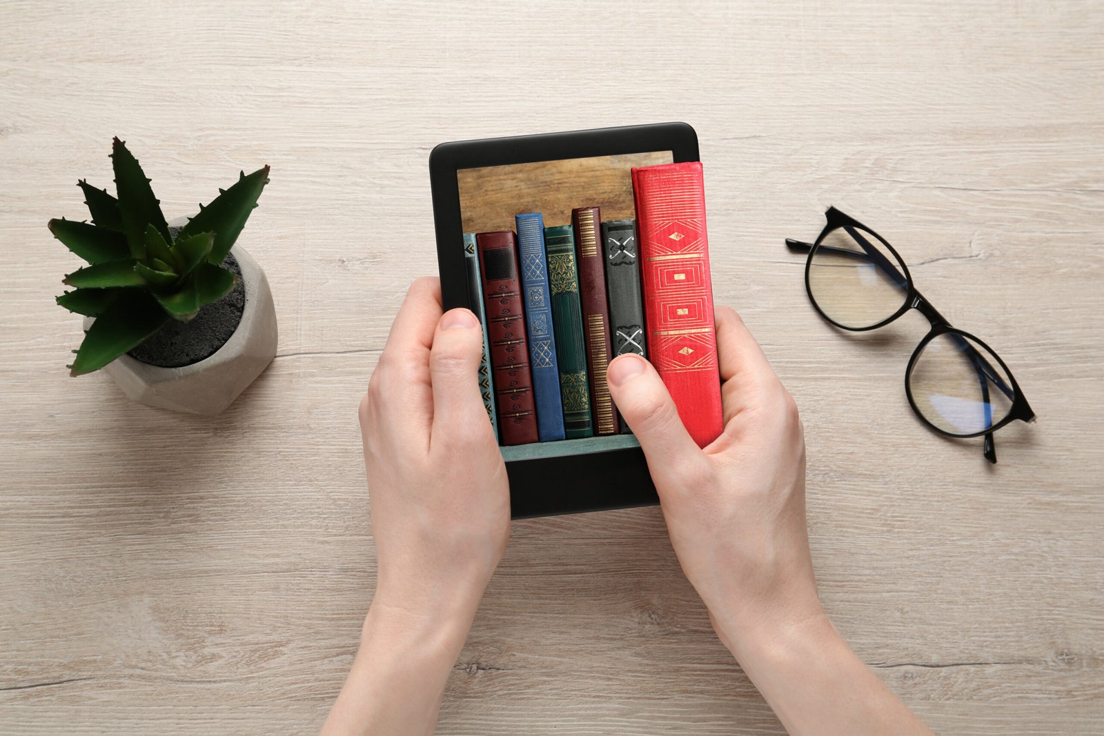 Woman using e-book reader at wooden table, top view